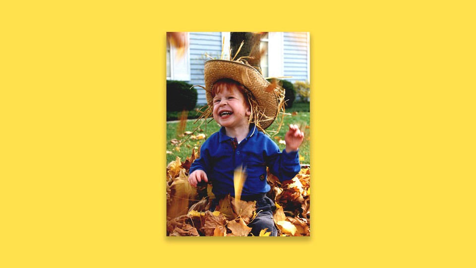 A young boy plays in a pile of leaves.