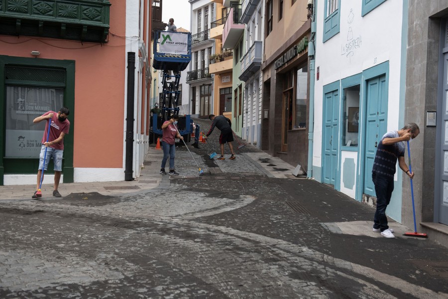 People sweep ash from a street.