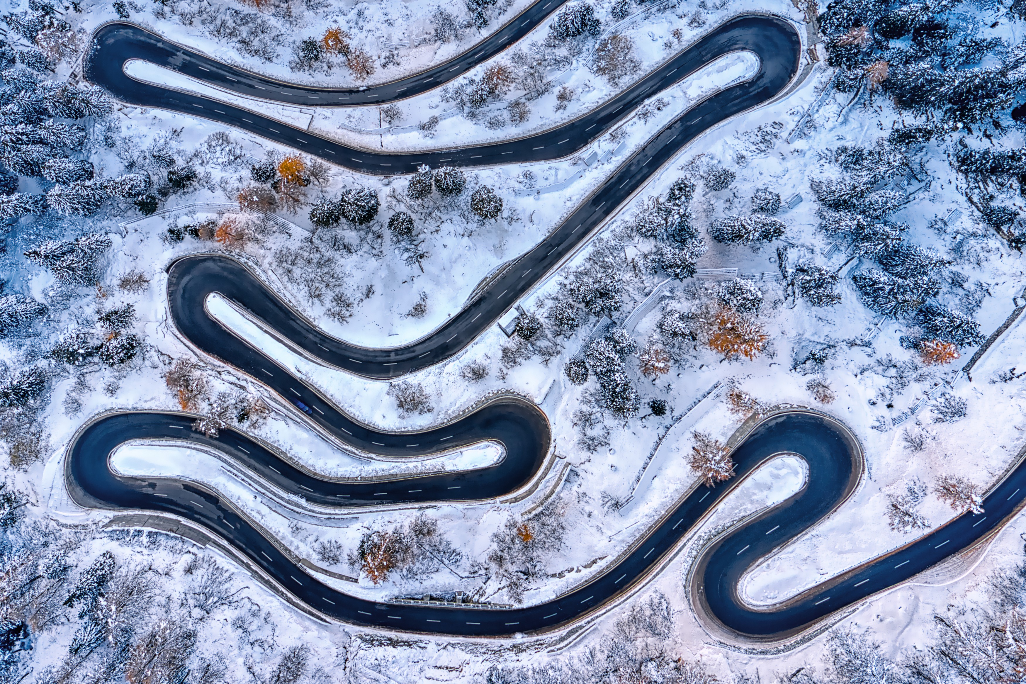 A view, from above, of a very twisty mountain road on a snow-covered slope