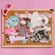 A cork bulletin board covered in Taylor Swift CDs, photos, and ephemera connected with pink string, with heart-shaped sunglasses hanging from one corner