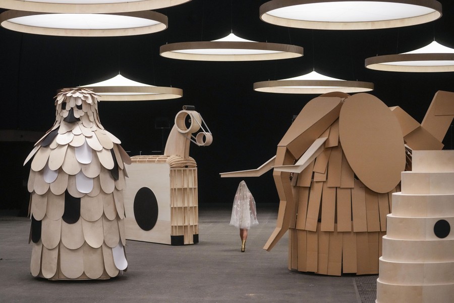A model walks among large wooden sculptures during a fashion show.