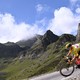 A cyclist rides down a road among mountain peaks.