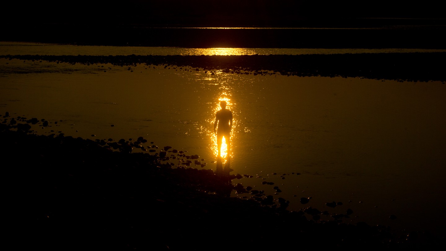 Silhouetted person and gleaming sun reflected on water
