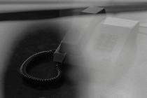 A black-and-white image of a woman's shadow over a desk. The desk has a phone and sunglasses on it.