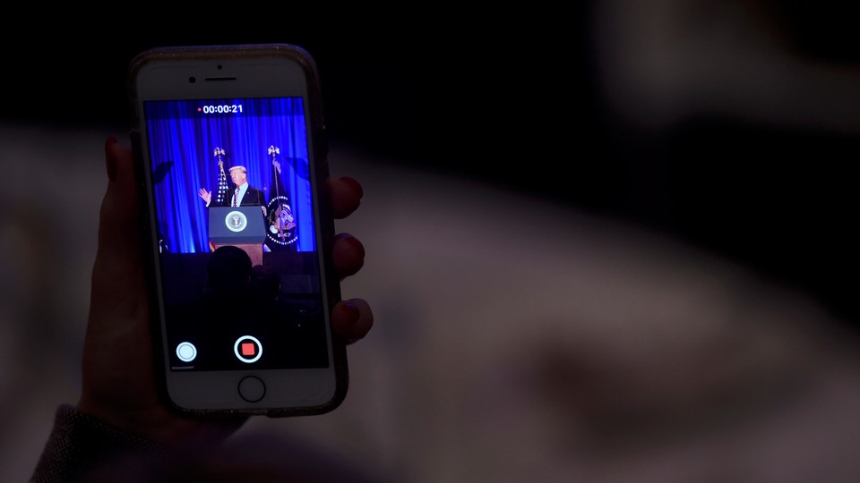 An audience member takes a video of President Donald Trump on her phone.