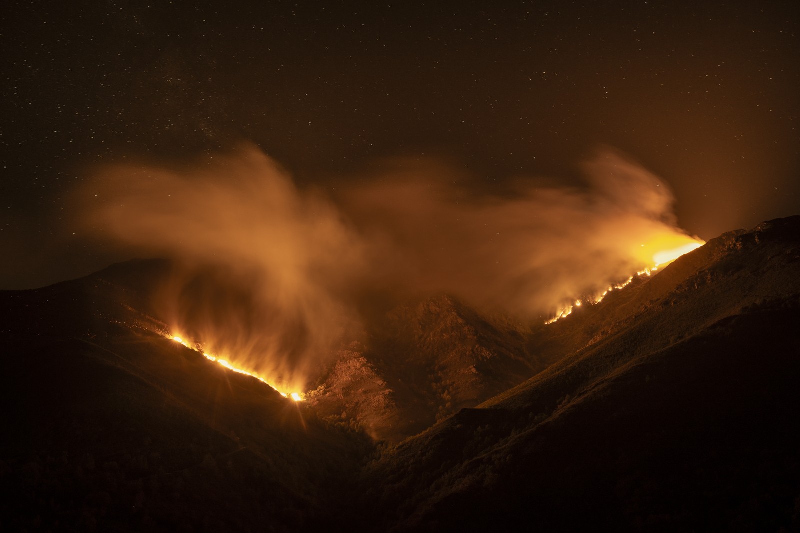 A wildfire burns along a hillside, seen at night.