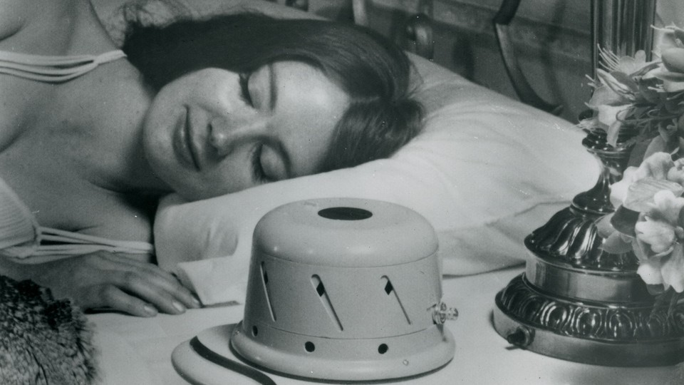 A black-and-white image of a woman sleeping next to a sound conditioner
