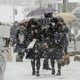 Students walk with umbrellas in the snow. 