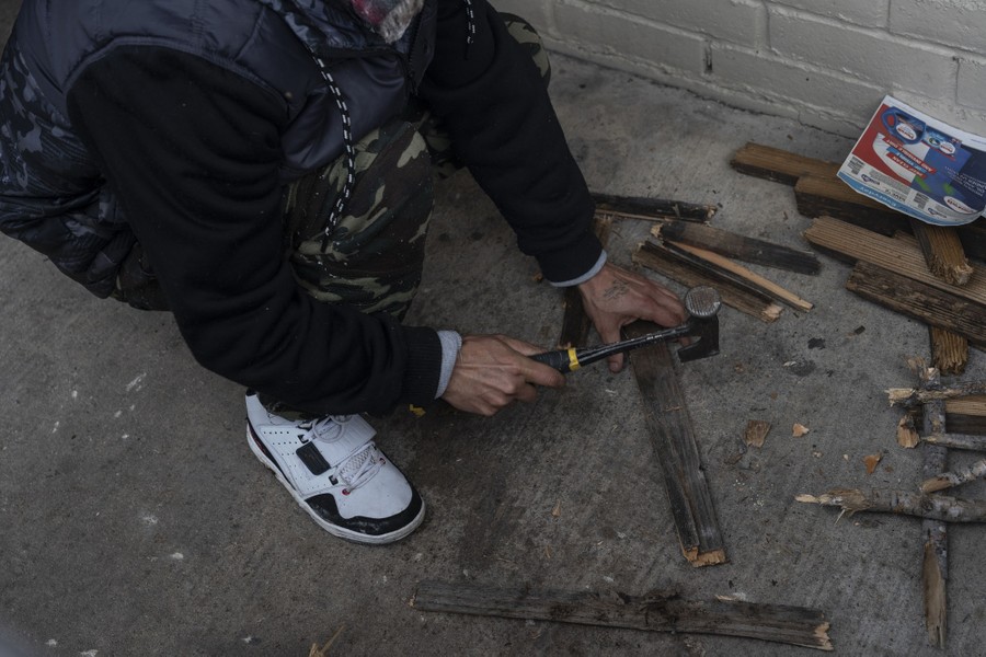 A person chops small bits of wood on concrete, using a hatchet.