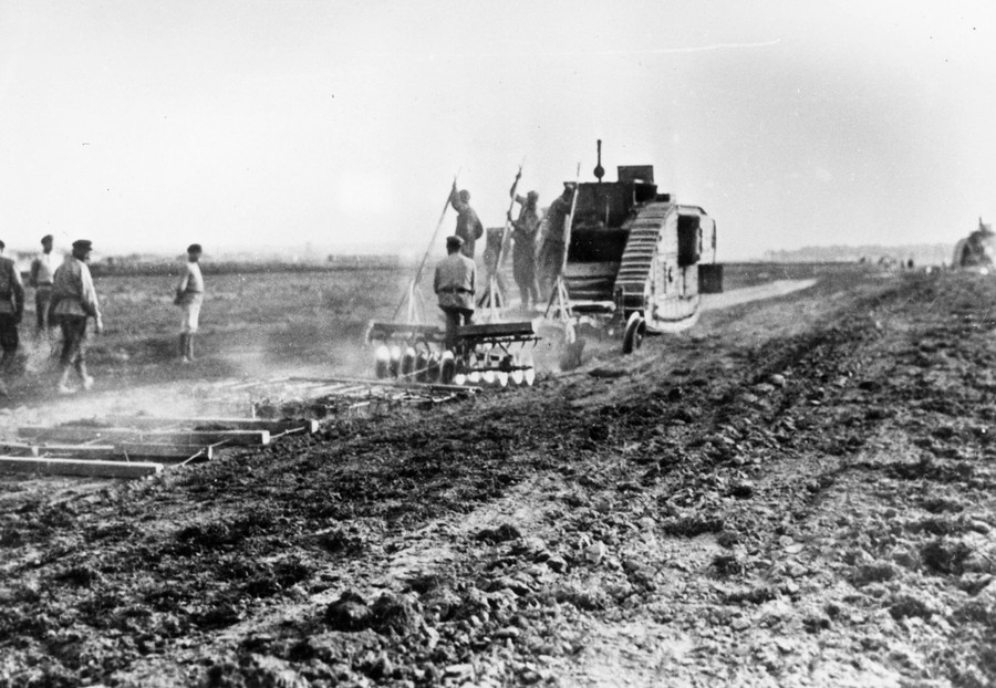 Men use a military tank to work a farm field.