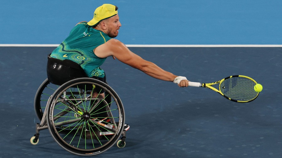 An athlete in a wheelchair reaches out to hit a tennis ball with his racket.