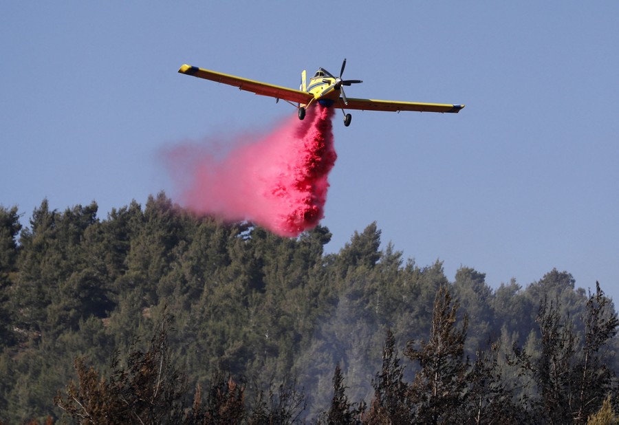 A small firefighting aircraft drops flame retardant onto a patch of forest.