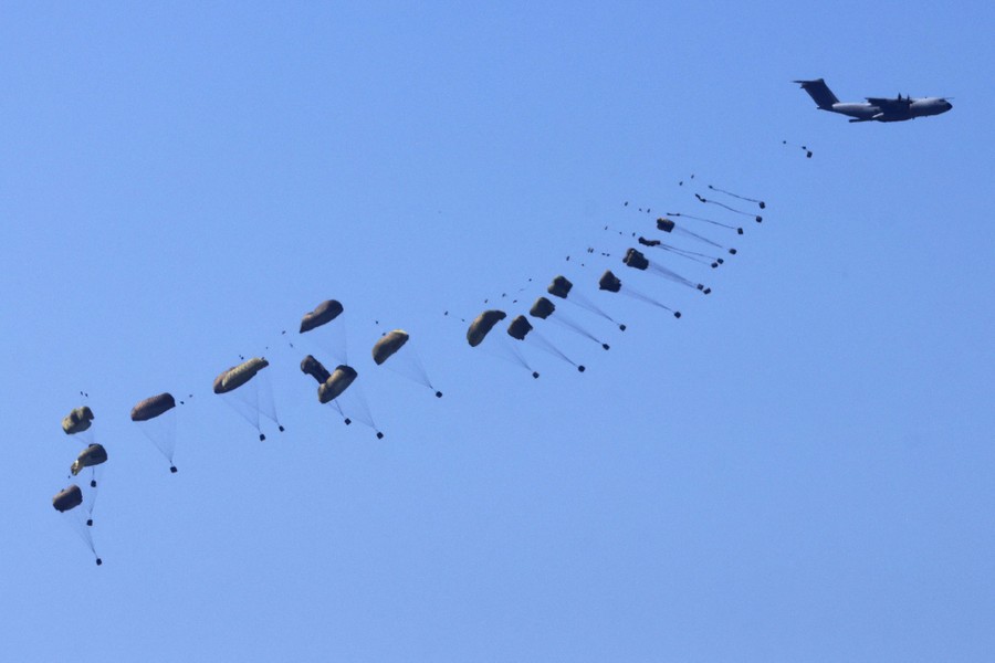 A military aircraft drops dozens of crates attached to parachutes.