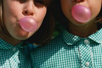 two girls wearing matching green gingham shirts and blowing pink gum bubbles