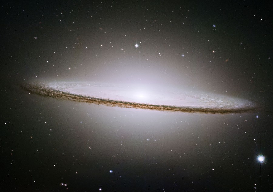A look at a spiral galaxy, seen edge-on, with a thick rim of dust encircling the bright center.