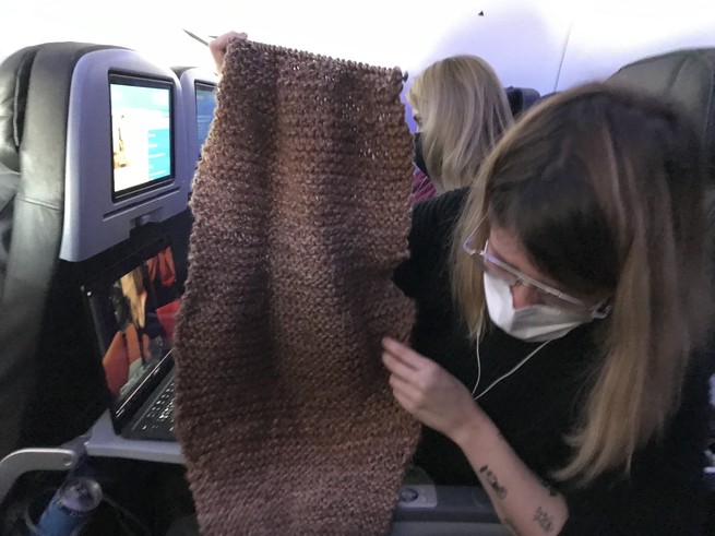 A woman holding up a deformed scarf on a plane.