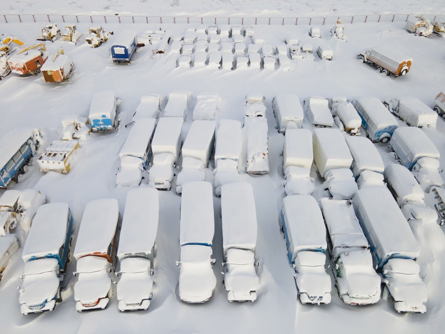 Snow-covered trucks and heavy equipment sit in a parking lot.