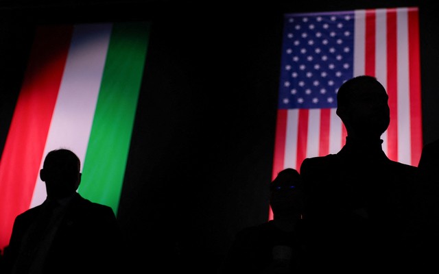 An image of two men standing in front of a U.S. flag and a Hungarian flag