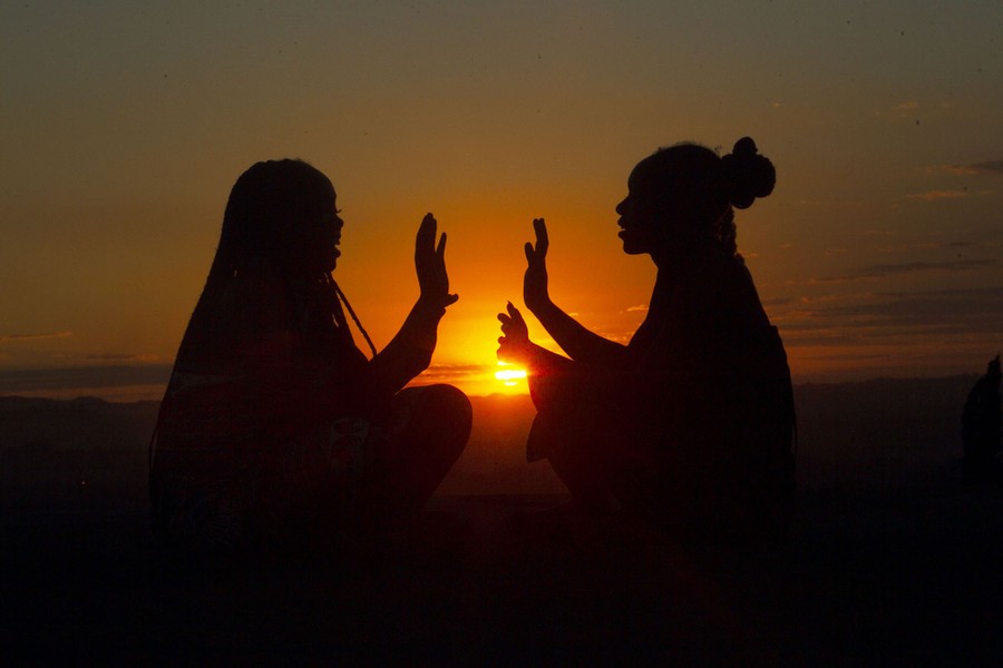 A silhouette of two girls playing together on a hill.
