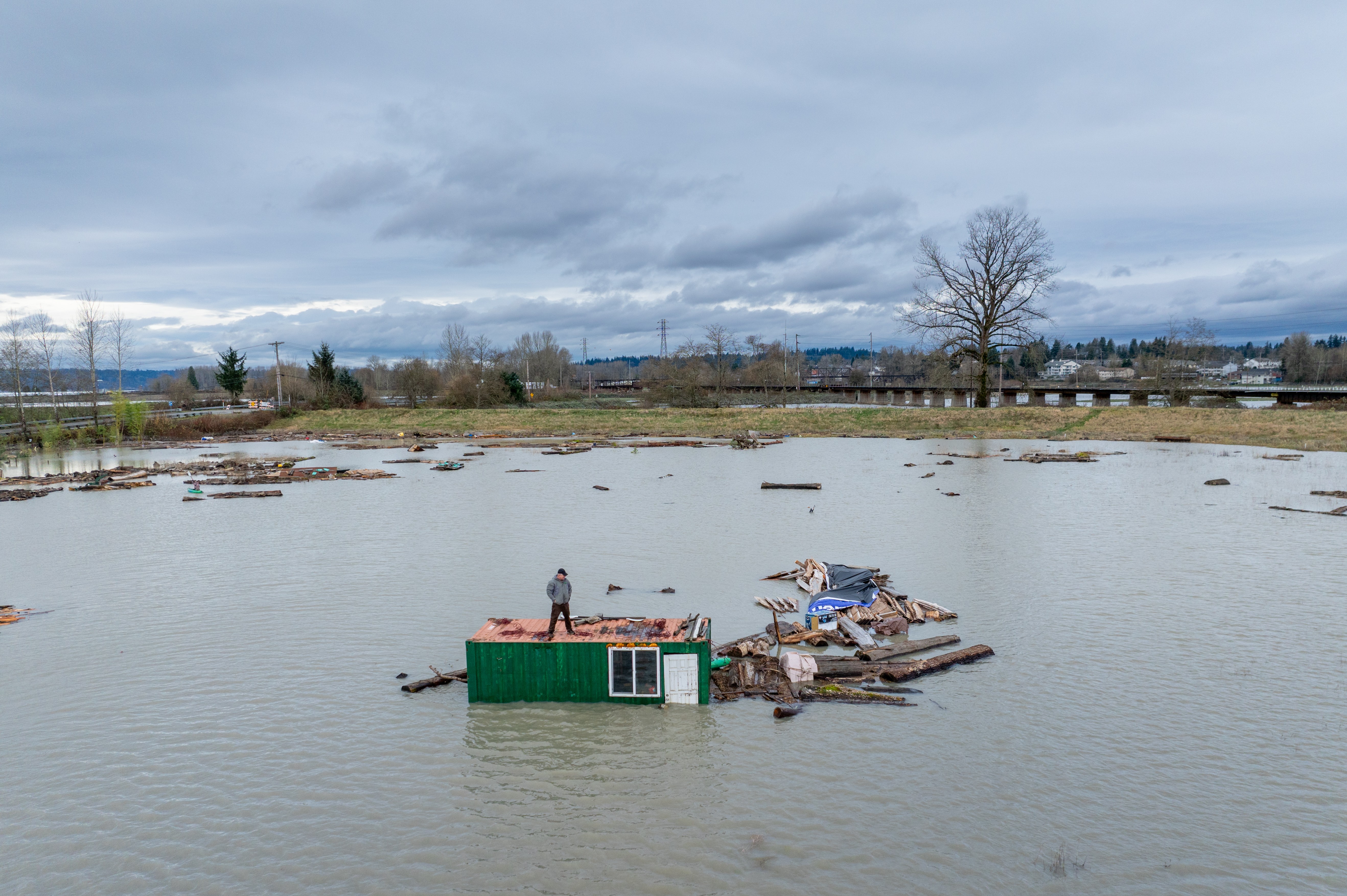 A person stands atop a small building engulfed by floodwater.