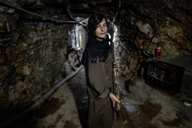 A woman stands with a rifle in an underground bunker