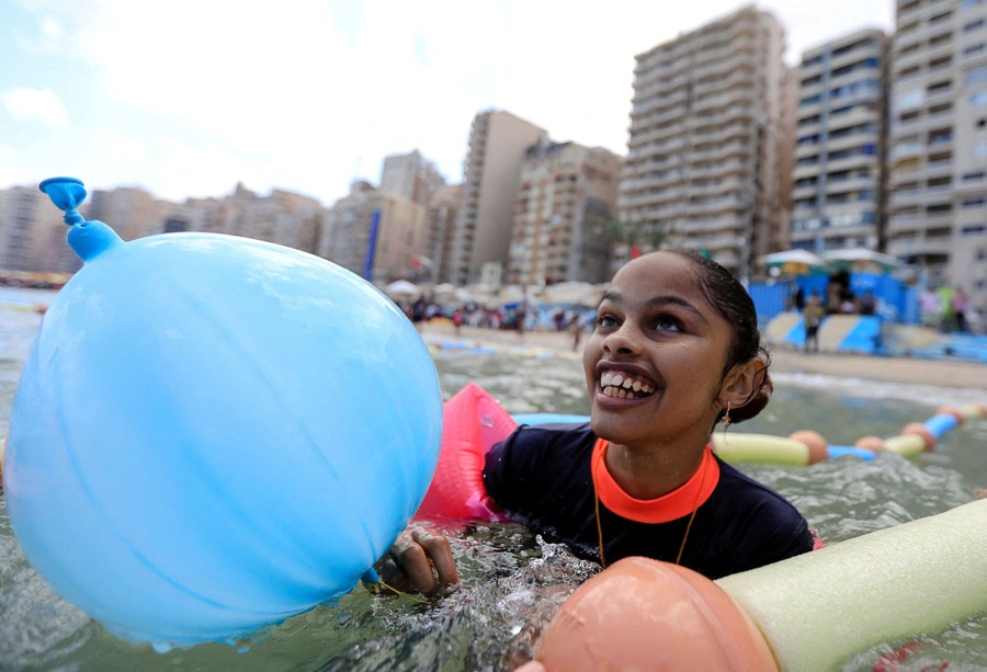 A young person splashes in shallow water at a beach, surrounded by floating aids.