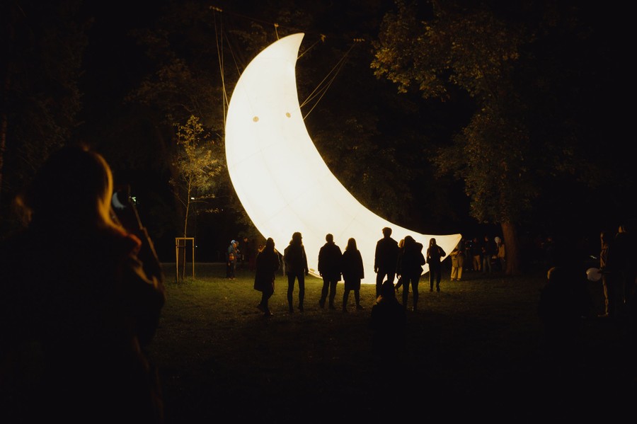 A small group of people stand in front of an installation shaped like a crescent moon.