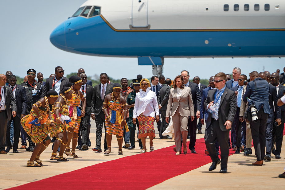 photo of Kamala Harris and group arriving on red carpet outdoors at airport with Air Force Two in background and women performing a greeting