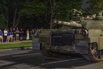 A group of young adults watches a tank roll through the street