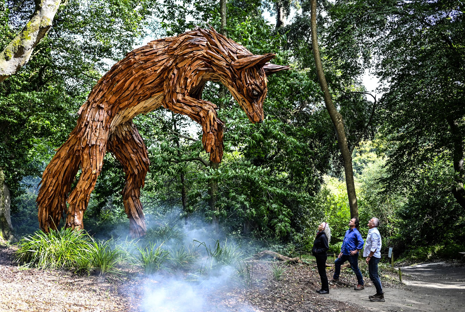 People look up toward a large sculpture of a leaping fox.