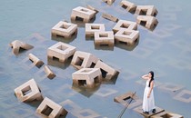 A woman stands on a cube-shaped concrete block, among many such blocks piled haphazardly in shallow water.