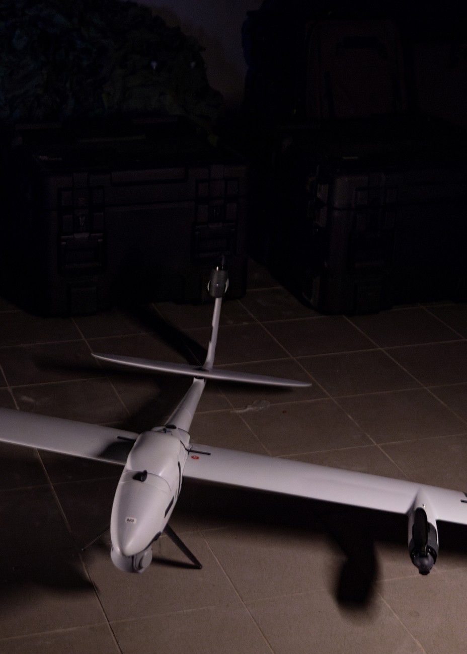 A white surveillance drone plan on the floor with a dark background.