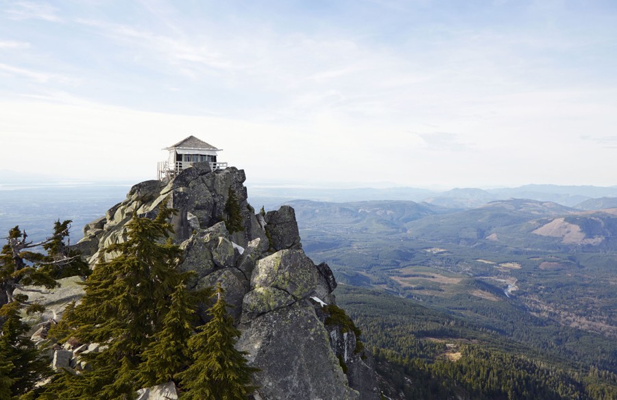 A fire-lookout tower stands on a rocky peak, overlooking a broad forested landscape.