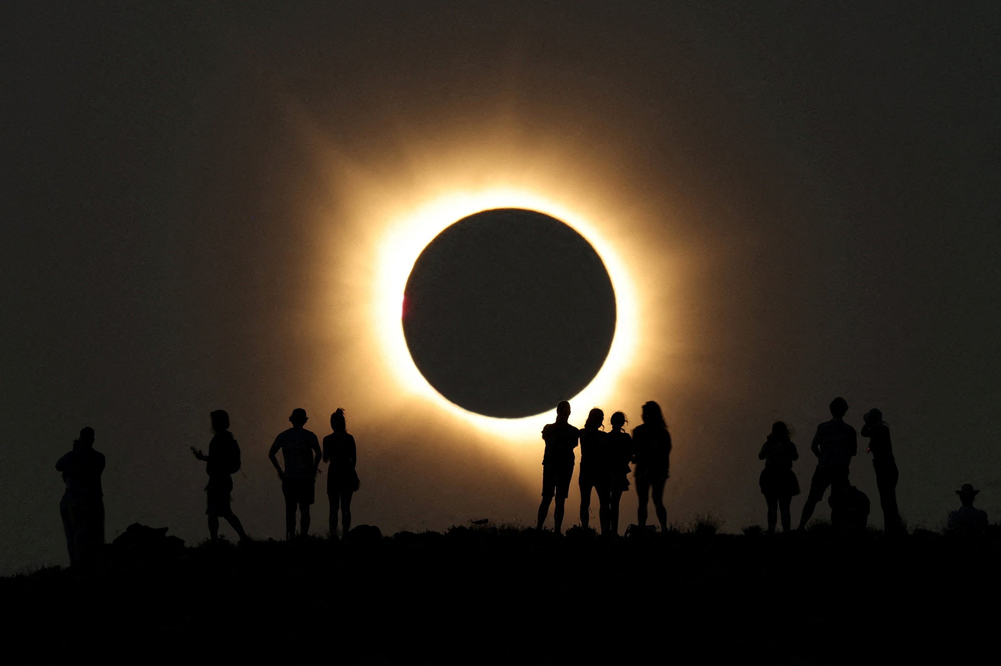 People stand on a ridge, backdropped by a total solar eclipse.