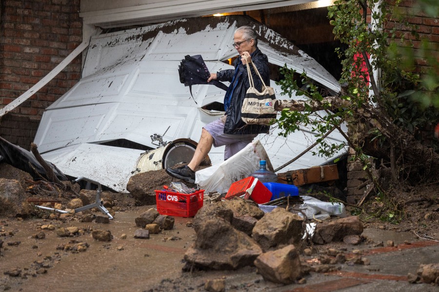 A person steps over debris outside a smashed and muddy garage.