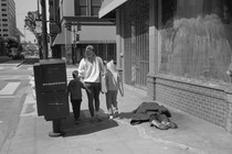 A family walks by a man laid out on the sidewalk