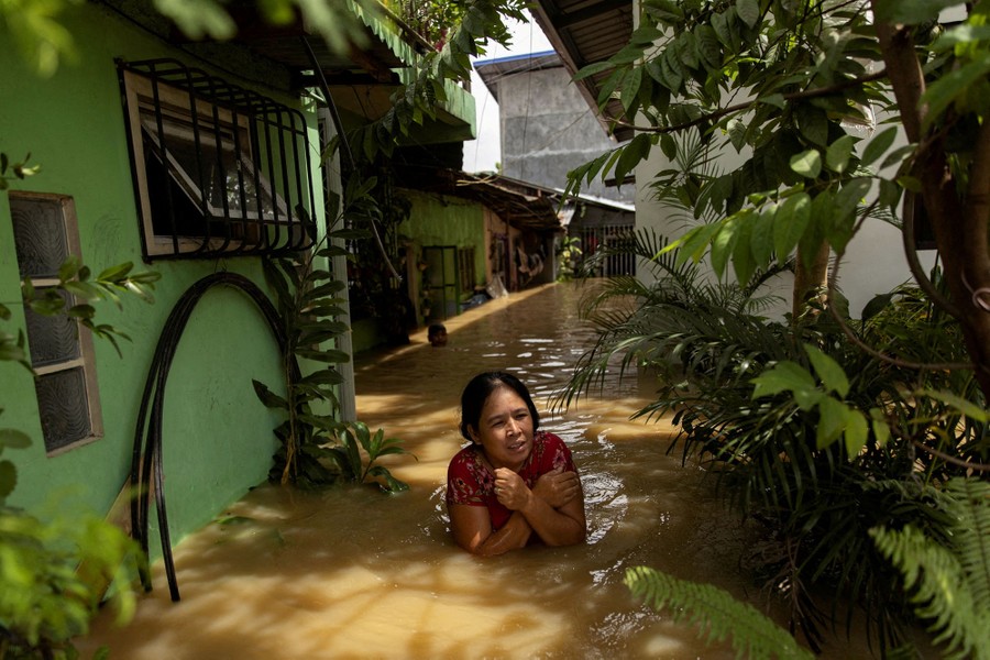 A woman wades through chest-deep floodwater near houses.