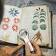 A man holds a magnifying glass over the Voynich Manuscript.