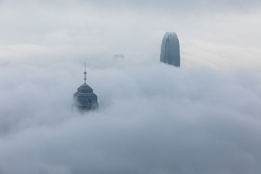 Several tall buildings poke out of low cloud cover.
