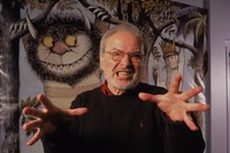 Maurice Sendak makes a gentle spooky gesture in front of his illustrations.