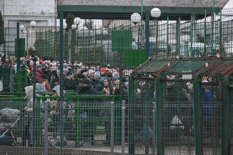 A large crowd of people stands together in line, surrounded by tall fences.