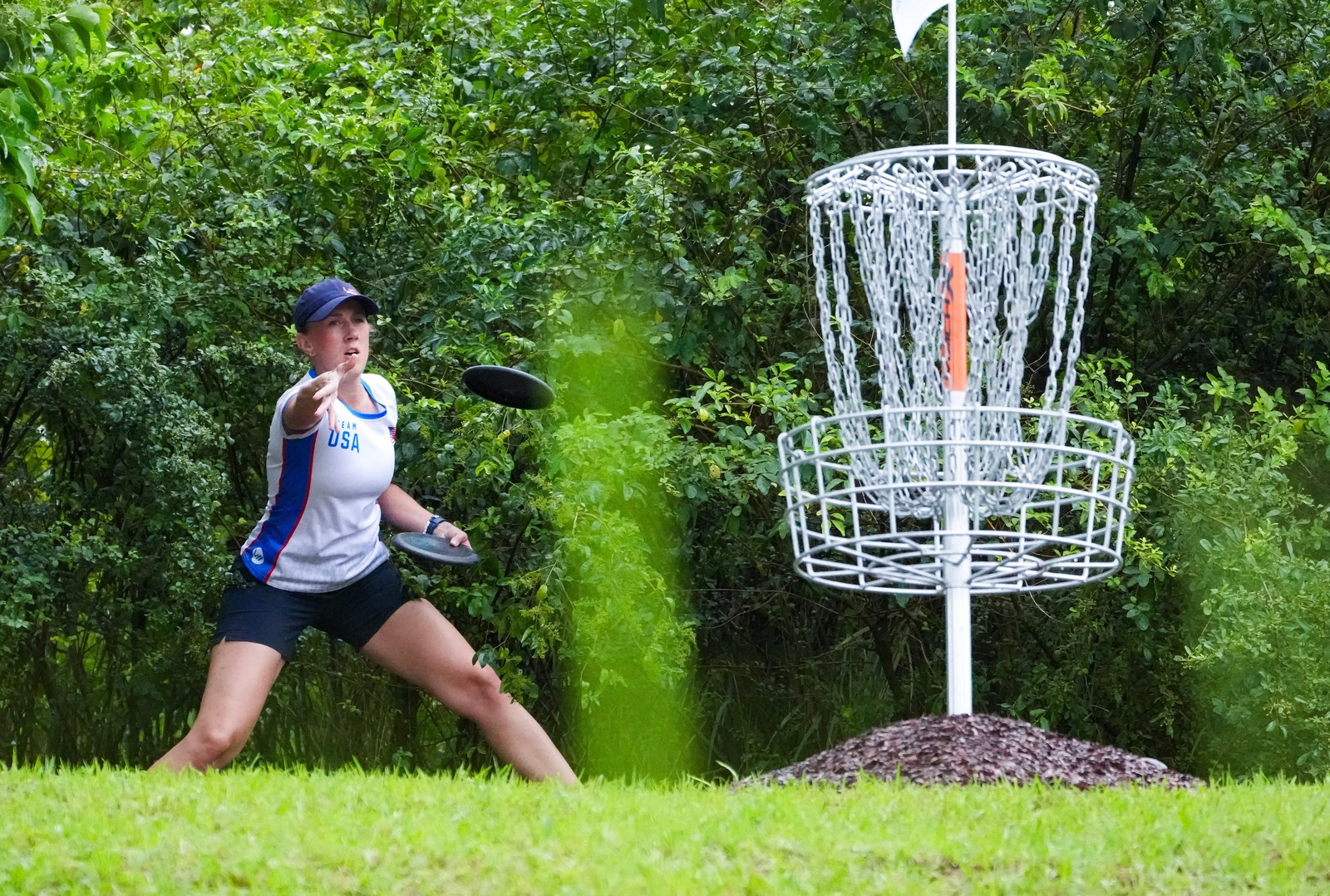 A person throws a disc toward a pole lined with chains during a disc golf competition.