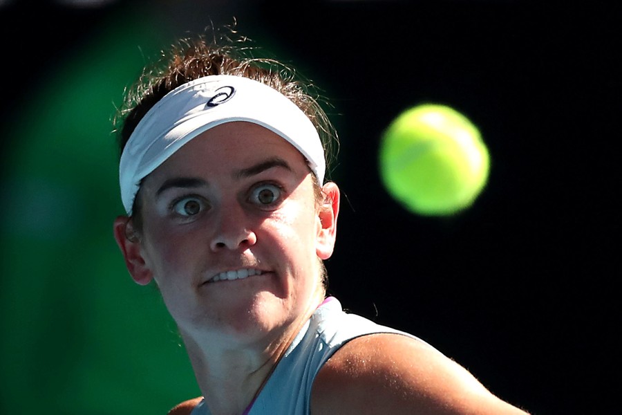 A woman looks at a flying tennis ball with concentration on her face.