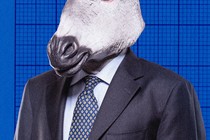 A businessman in a suit is shown wearing a donkey mask.