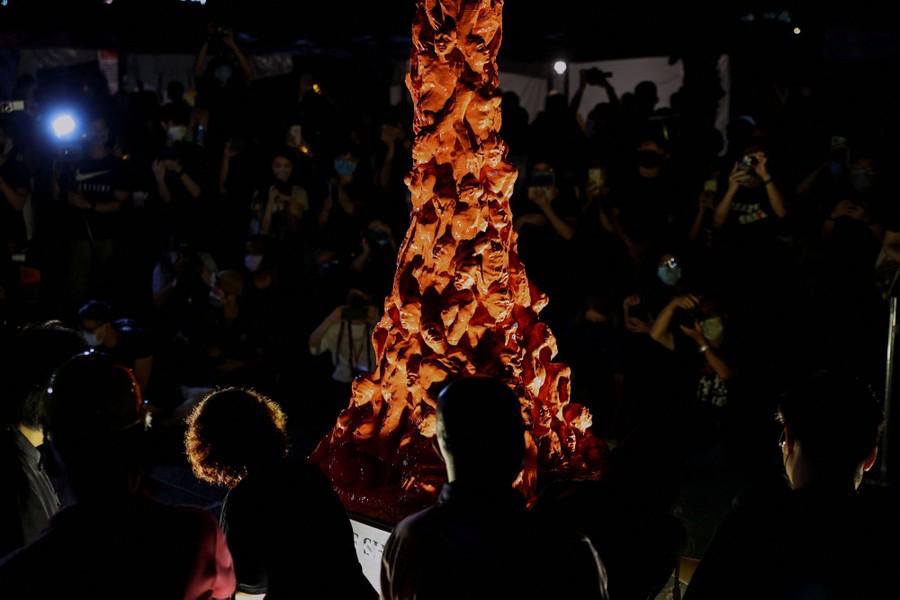 People take photos of a tall sculpture depicting twisted human bodies piled an top of each other.