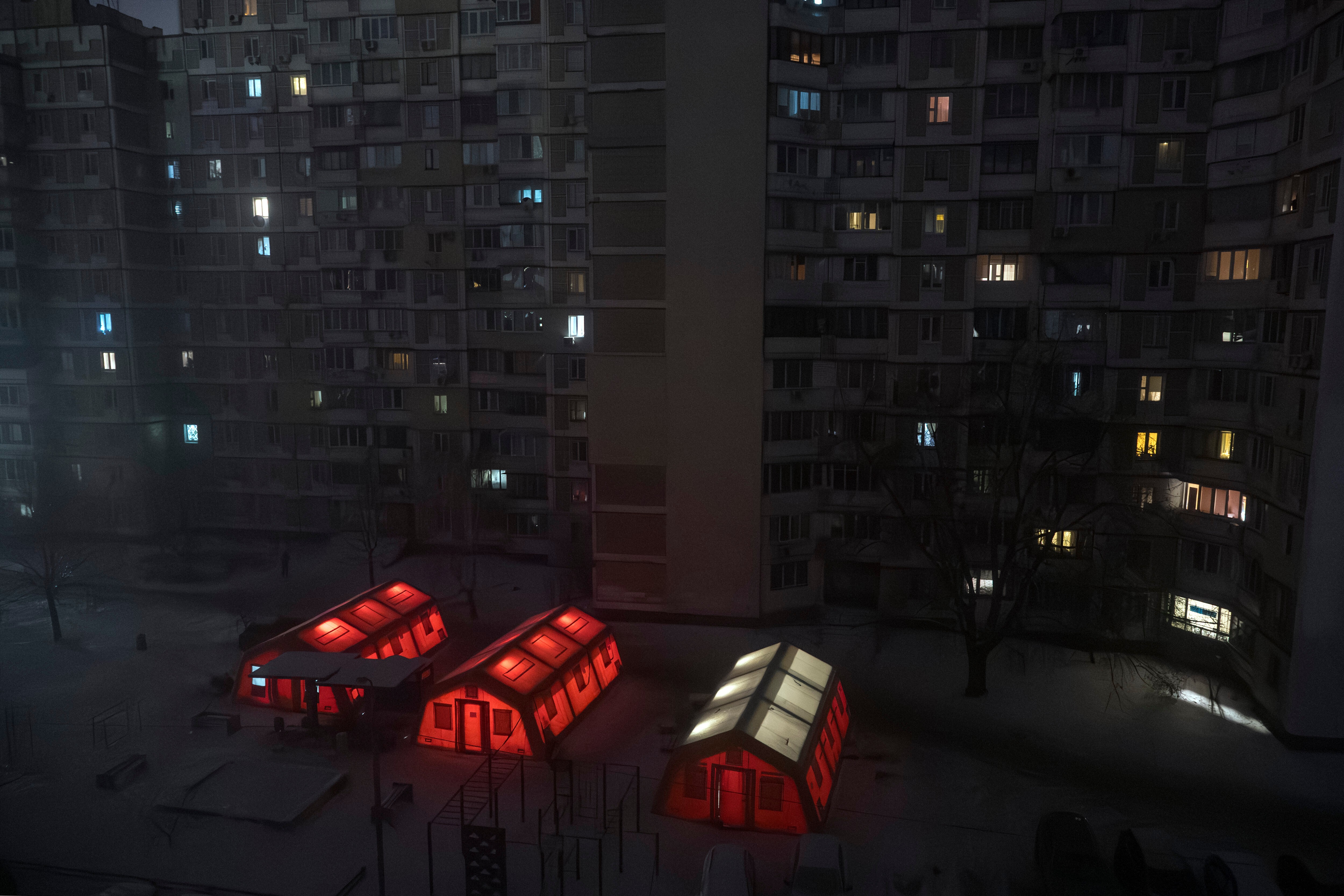 Three tents, glowing with red light, stand beneath tall residential buildings.
