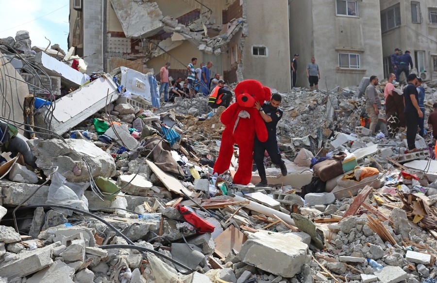 A large stuffed bear is carried from the debris of a destroyed building.