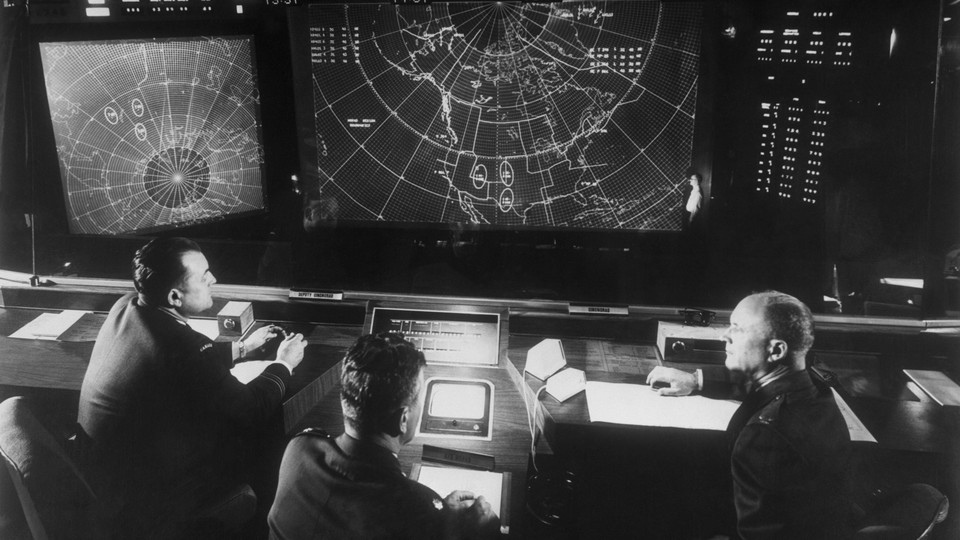 A black-and-white photograph of a group of people looking at a screen displaying a map of the United States