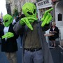 Two people dressed in green alien heads and hands gesture on a busy street.