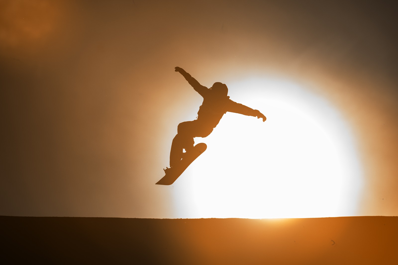 A snowboarder, seen in silhouette, mid-jump